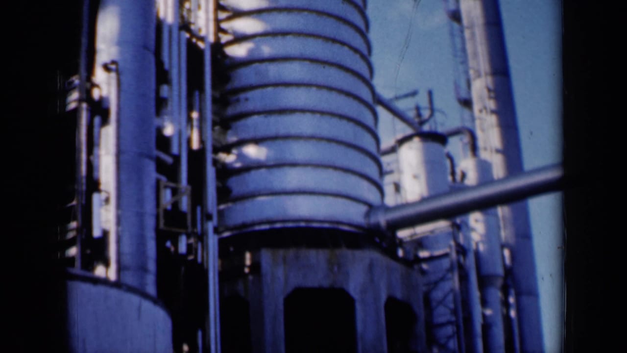 Tall industrial tanks and pipework seen from below against blue sky.
