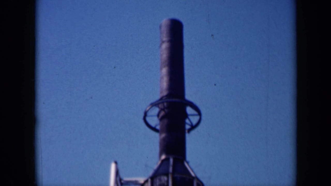 1961 Missouri 8mm frame showing the upper section of a dark cylindrical tower or rocket-like structure against clear sky.