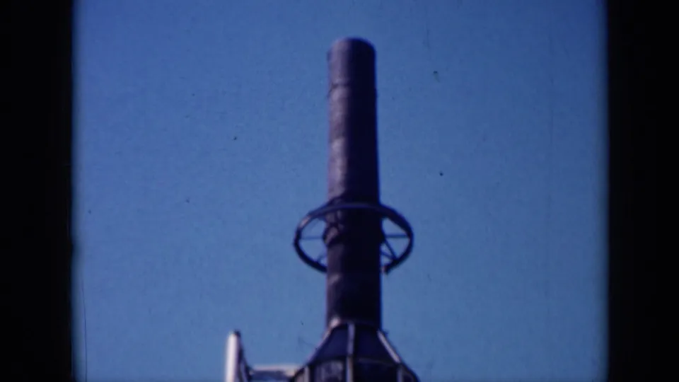 1961 Missouri 8mm frame showing the upper section of a dark cylindrical tower or rocket-like structure against clear sky.