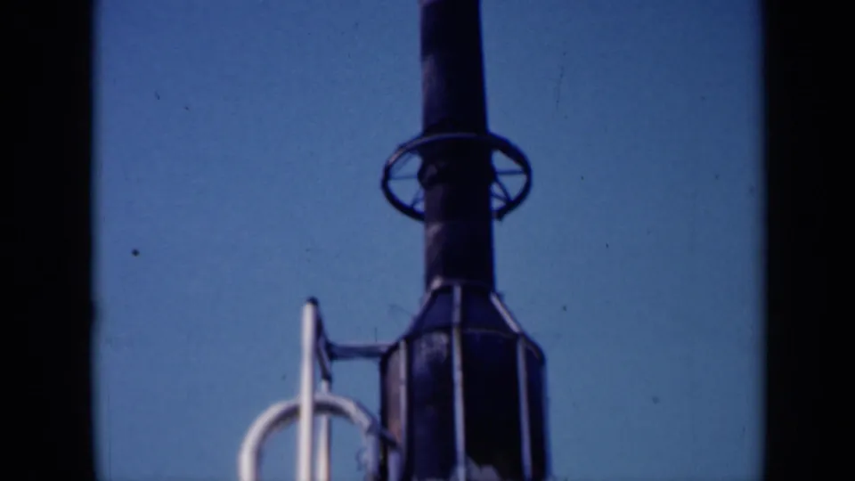1961 Missouri 8mm frame showing a dark launch-tower or rocket-like structure with pale support piping and rail details.