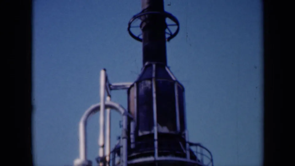 1961 Missouri 8mm frame showing a rocket-like vertical structure, circular rings, railings, and adjacent support pipe against blue sky.
