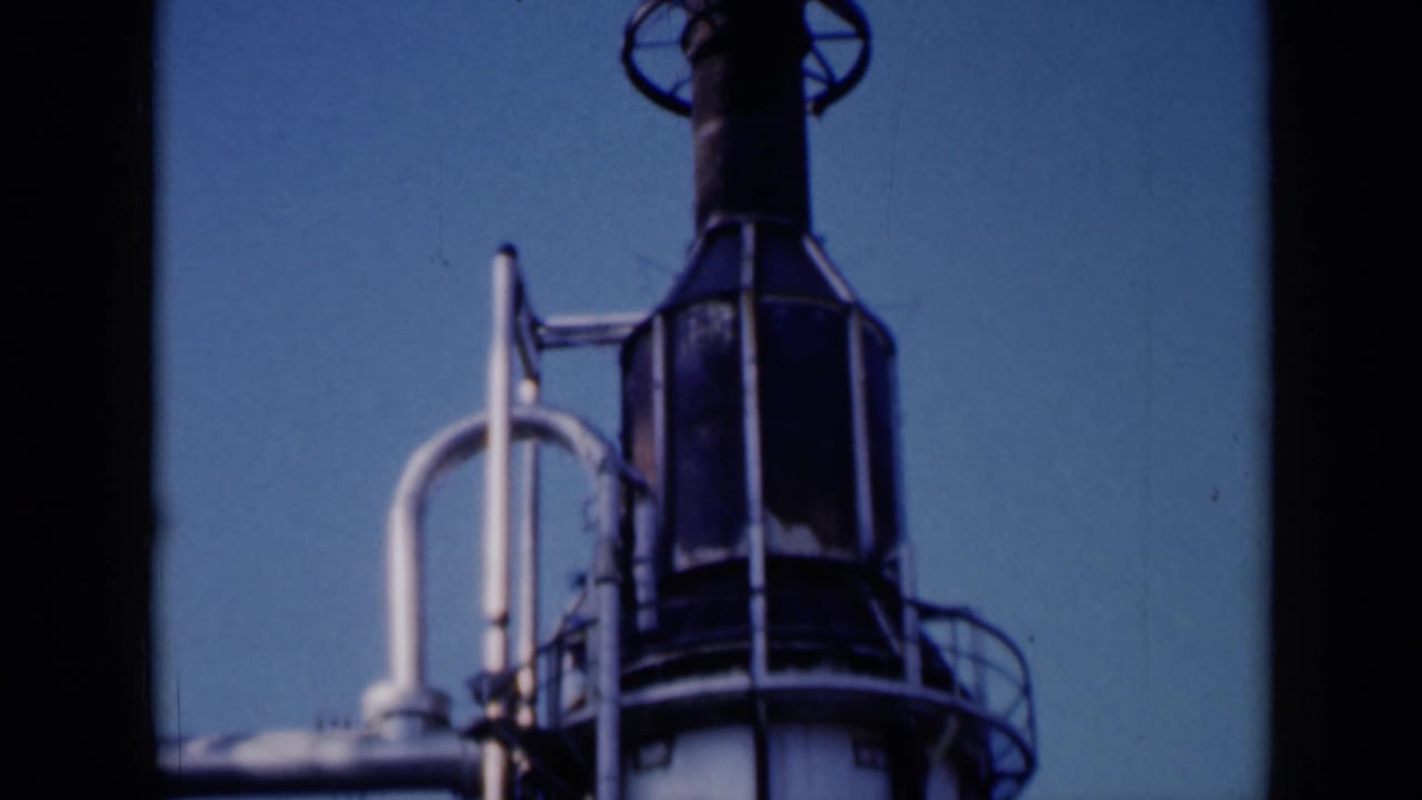 Tall white industrial tower with dark top section and exterior piping against blue sky.