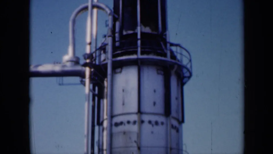 1961 Missouri home-movie view looking down the same tall industrial tower, with the white cylinder, weathered panels, railings and pipework visible.