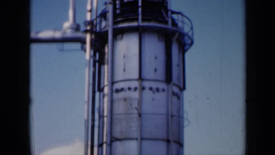 1961 Missouri frame showing a closer lower section of the industrial tower, with ring railings, vertical piping and soft 8mm film texture.