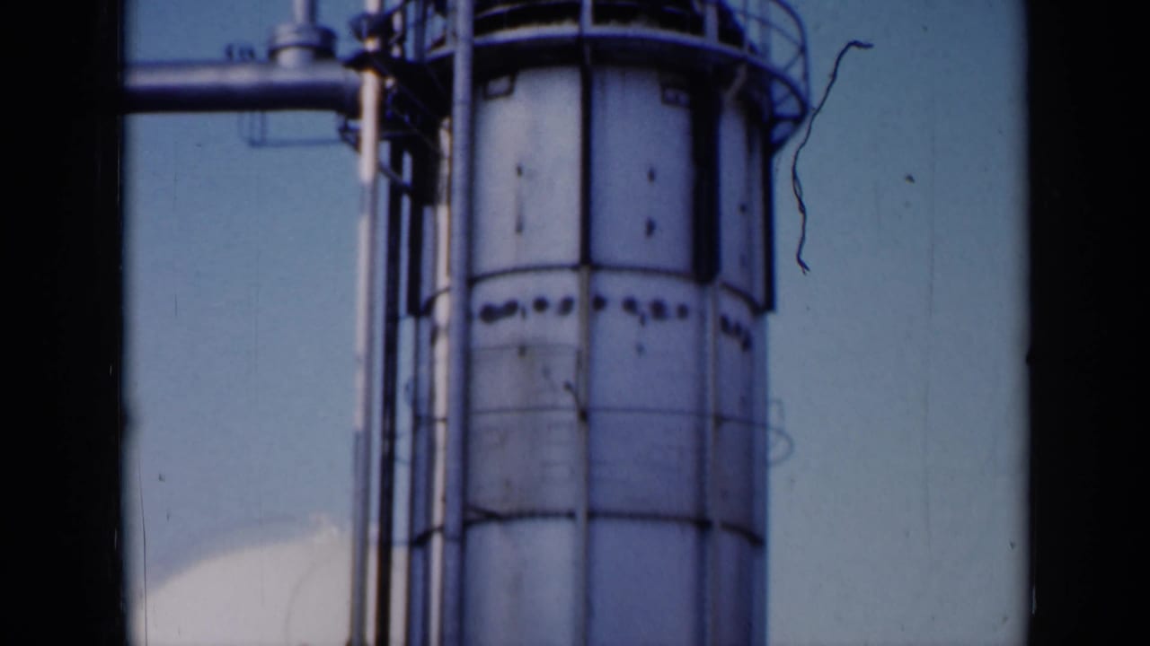 Tall white cylindrical industrial tank with pipes and railings against a clear sky.