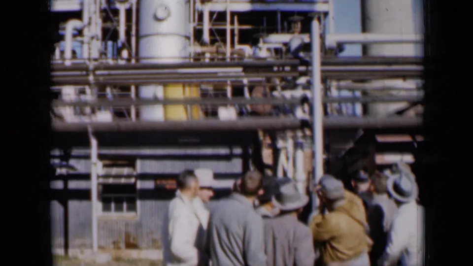 1961 Missouri 8mm frame with men gathered under pipe runs and railings during an apparent industrial facility tour.