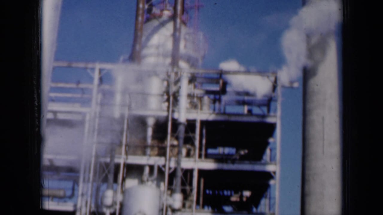 1961 Missouri 8mm frame showing an industrial facility with metal platforms, tanks, and white plumes rising near smokestacks.