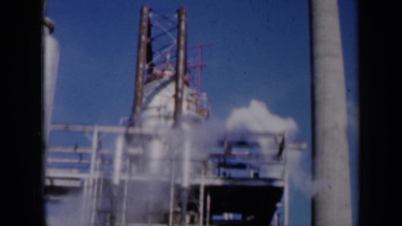 Smokestack and factory platforms with a white plume moving across the frame.