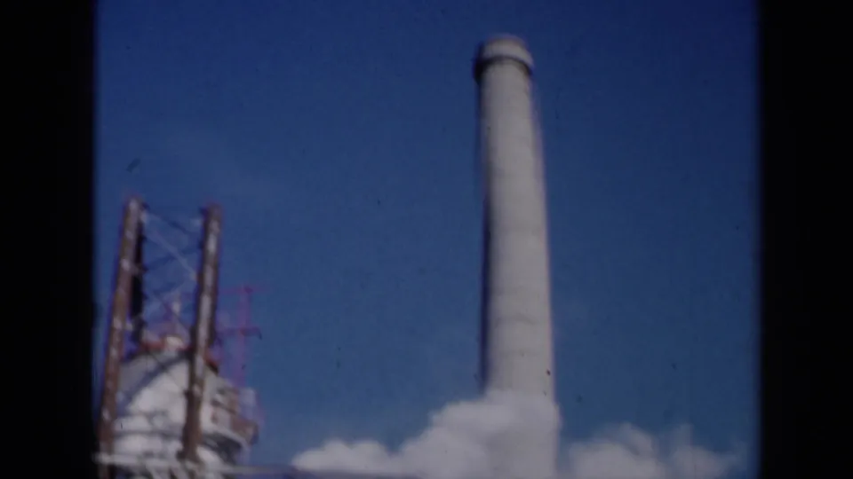 1961 Missouri 8mm frame showing a tall stack, adjacent industrial tower, and drifting white steam or smoke plumes.