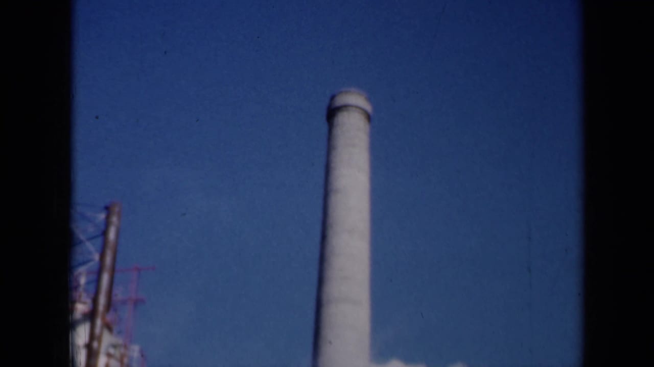 1961 Missouri industrial exterior showing a tall smokestack against blue sky with partial structures at the edge of frame.