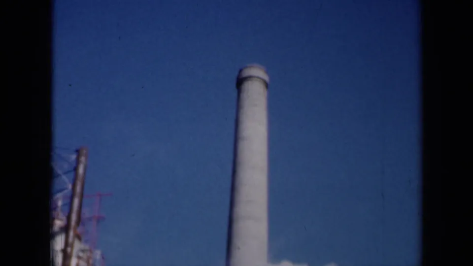 1961 Missouri industrial exterior showing a tall smokestack against blue sky with partial structures at the edge of frame.