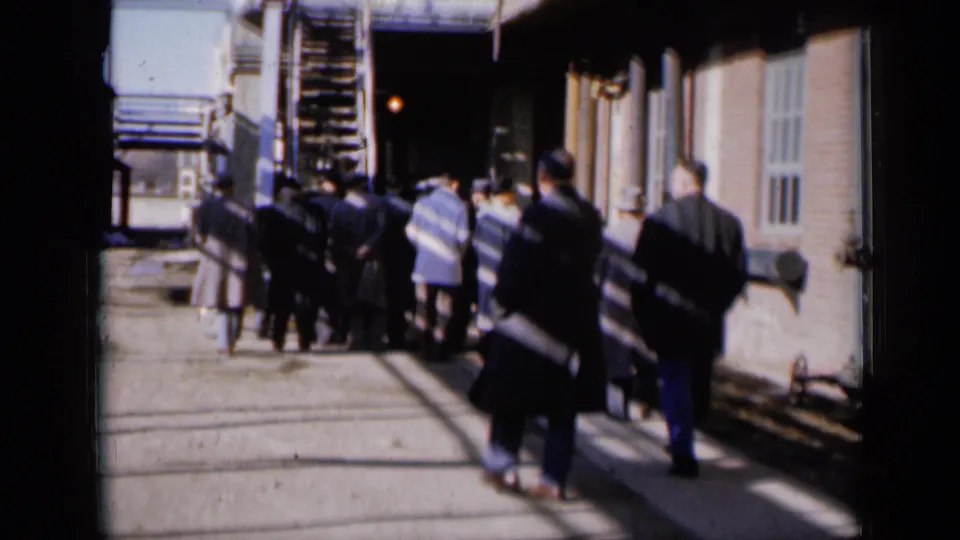 Men walk away through a sunlit Missouri industrial alley in 1961, framed by brick walls, metal stairs, and high-contrast shadows.
