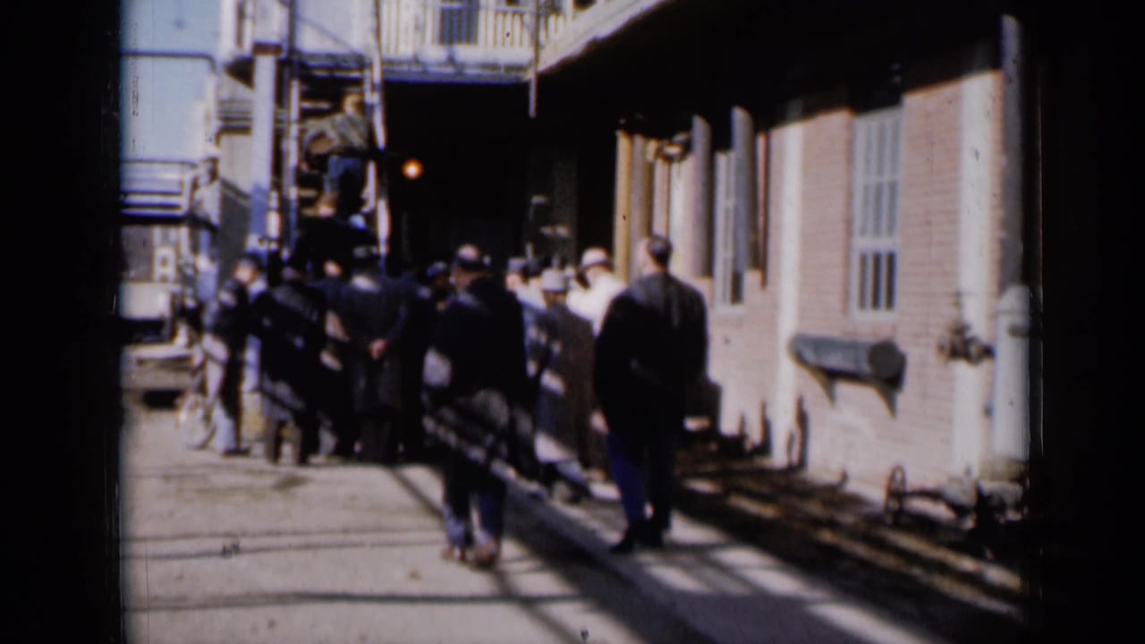 A group of men stands near a staircase, with several figures beginning to move toward the steps.