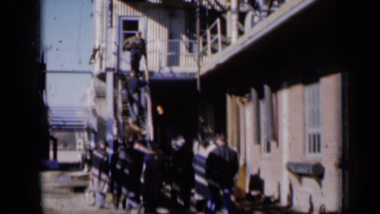 Adults gather near a brick building while several people stand on an exterior metal stair.