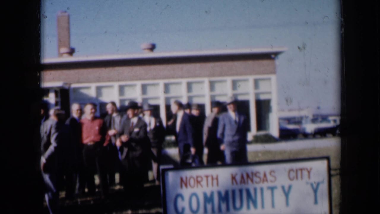 Adults in formal clothing stand outside a building behind a North Kansas City Community Y sign.