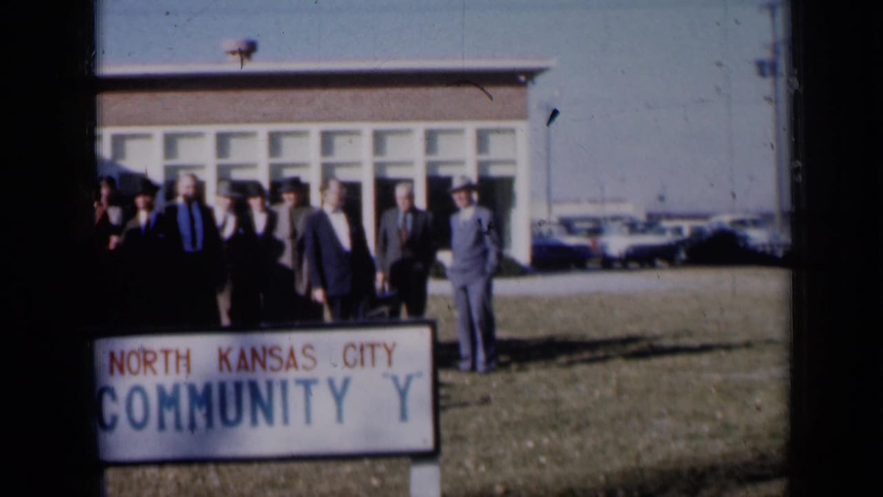 Formally dressed adults gather on a lawn beside a North Kansas City Community Y sign.