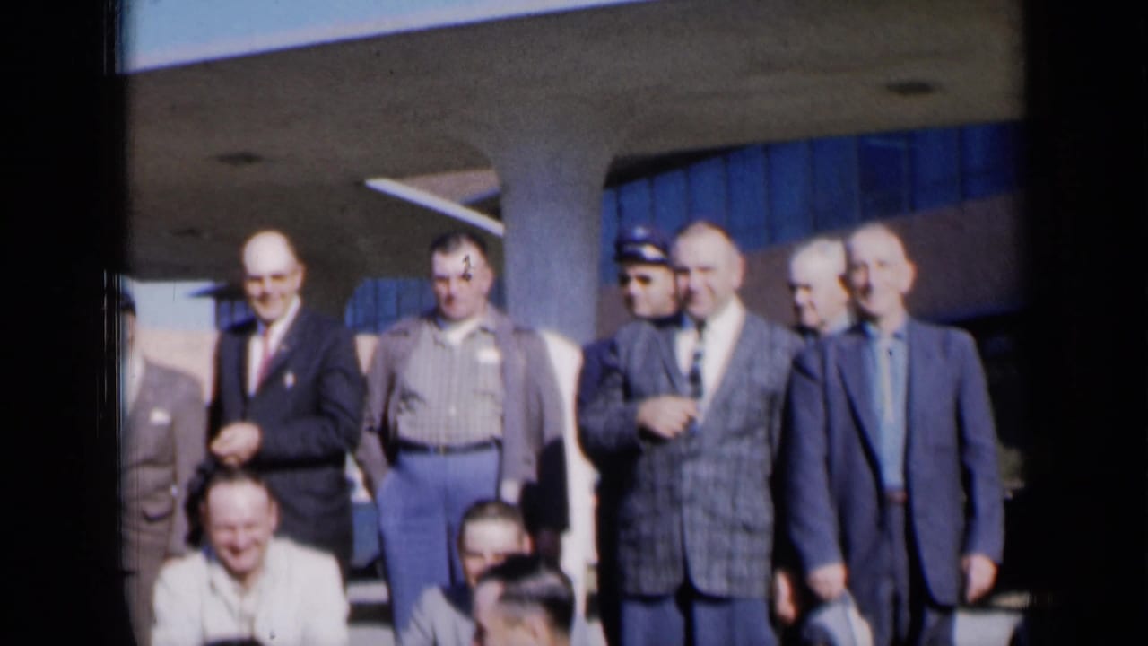 A line of men stands outside, including one in a plaid jacket and another wearing a cap.