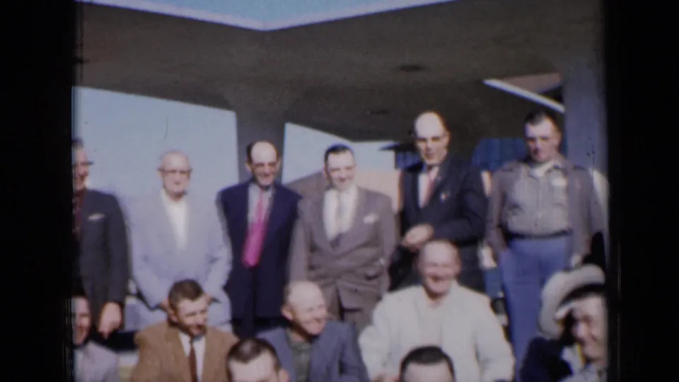 Final frame shows a broader adult male group outside a modern Missouri building, mixing formal suits and casual shirts.
