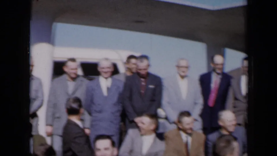 Men in suits and ties gather near a white vehicle and columned building in a 1961 Missouri home-movie frame.