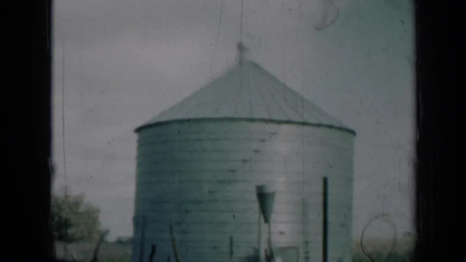 1961 Missouri home-movie frame showing a grey corrugated metal silo with a conical roof, partly framed by dark foreground edges.