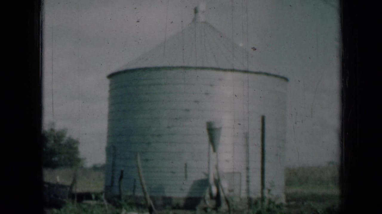 1961 Missouri 8mm frame showing the lower portion of a grey farm silo, nearby posts, vegetation and soft home-movie grain.