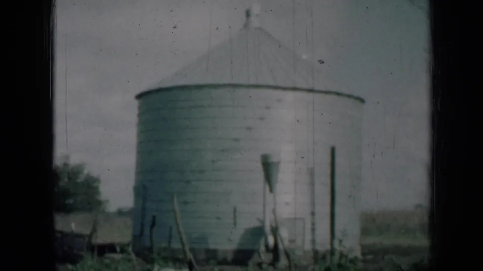 1961 Missouri 8mm frame showing the lower portion of a grey farm silo, nearby posts, vegetation and soft home-movie grain.