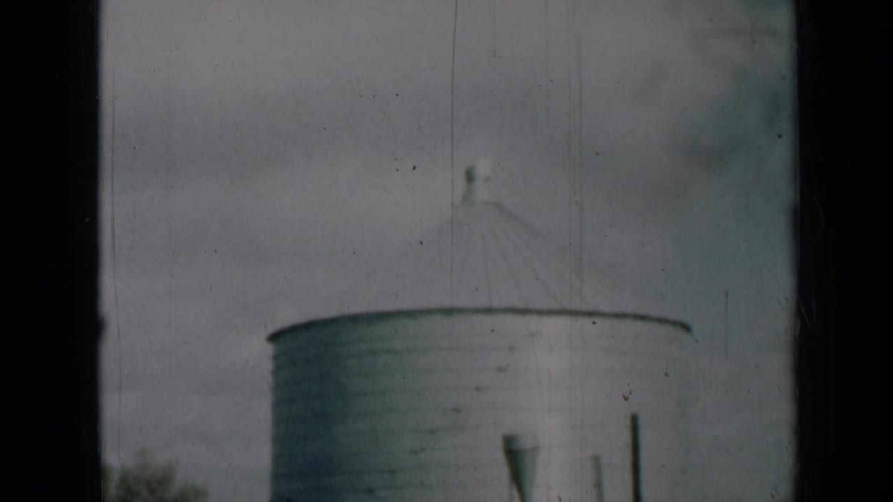 Soft 8mm frame from rural Missouri showing the upper section of an aluminum silo and its conical roof against clouds.