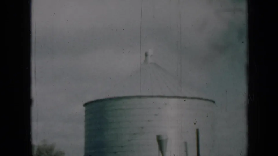 Soft 8mm frame from rural Missouri showing the upper section of an aluminum silo and its conical roof against clouds.