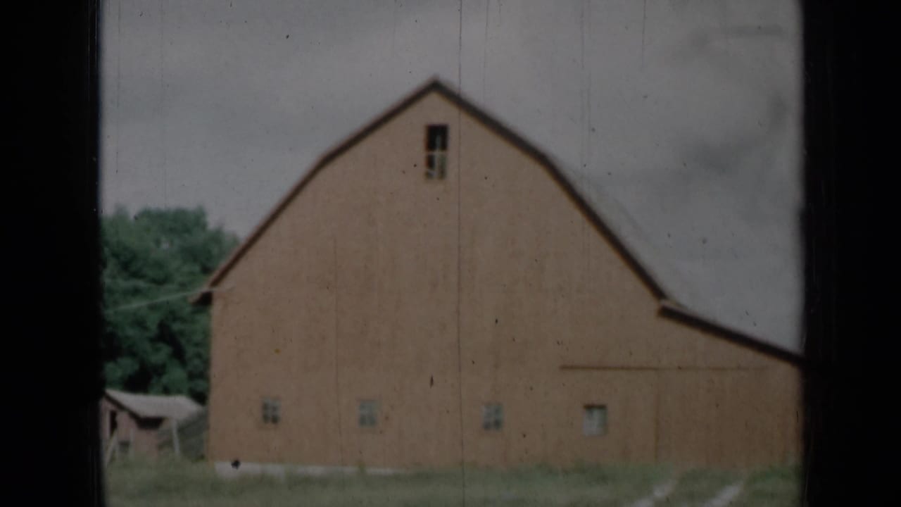 1961 Missouri 8mm frame showing a red rural barn with a gambrel roof, small windows, grass, trees, and cloudy sky.