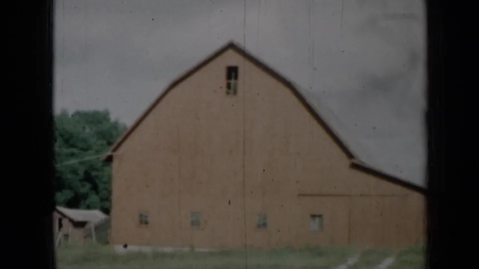 1961 Missouri 8mm frame showing a red rural barn with a gambrel roof, small windows, grass, trees, and cloudy sky.