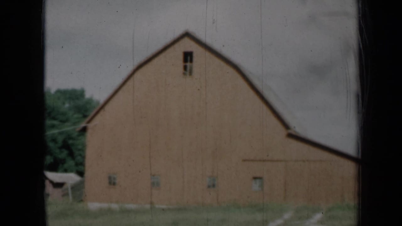 1961 Missouri 8mm frame showing a red-brown barn with a gambrel roof, small windows, grass, trees, and dark window bars in the foreground.