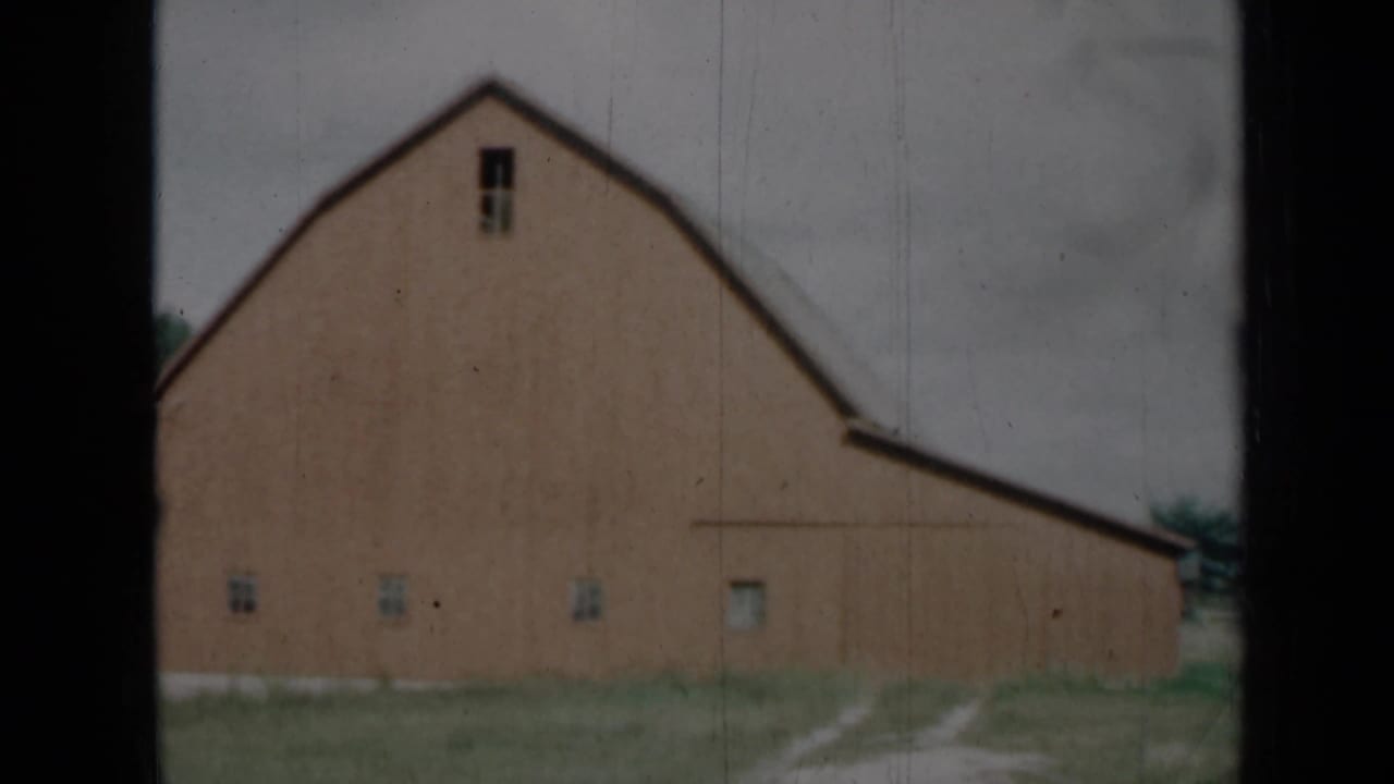 1961 Missouri 8mm frame with a closer look at the barn wall, gambrel roofline, small windows, grassy ground, and dark frame edges.