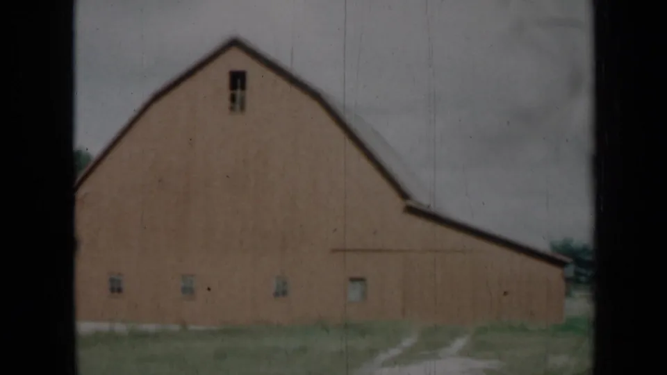 1961 Missouri 8mm frame with a closer look at the barn wall, gambrel roofline, small windows, grassy ground, and dark frame edges.
