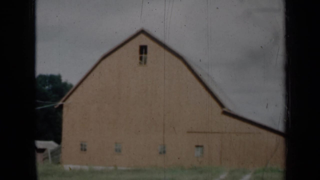 1961 Missouri 8mm view of a large red barn with small windows, grass foreground and overcast sky.