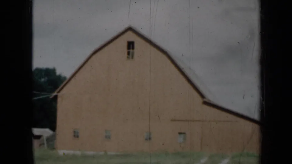 1961 Missouri 8mm view of a large red barn with small windows, grass foreground and overcast sky.