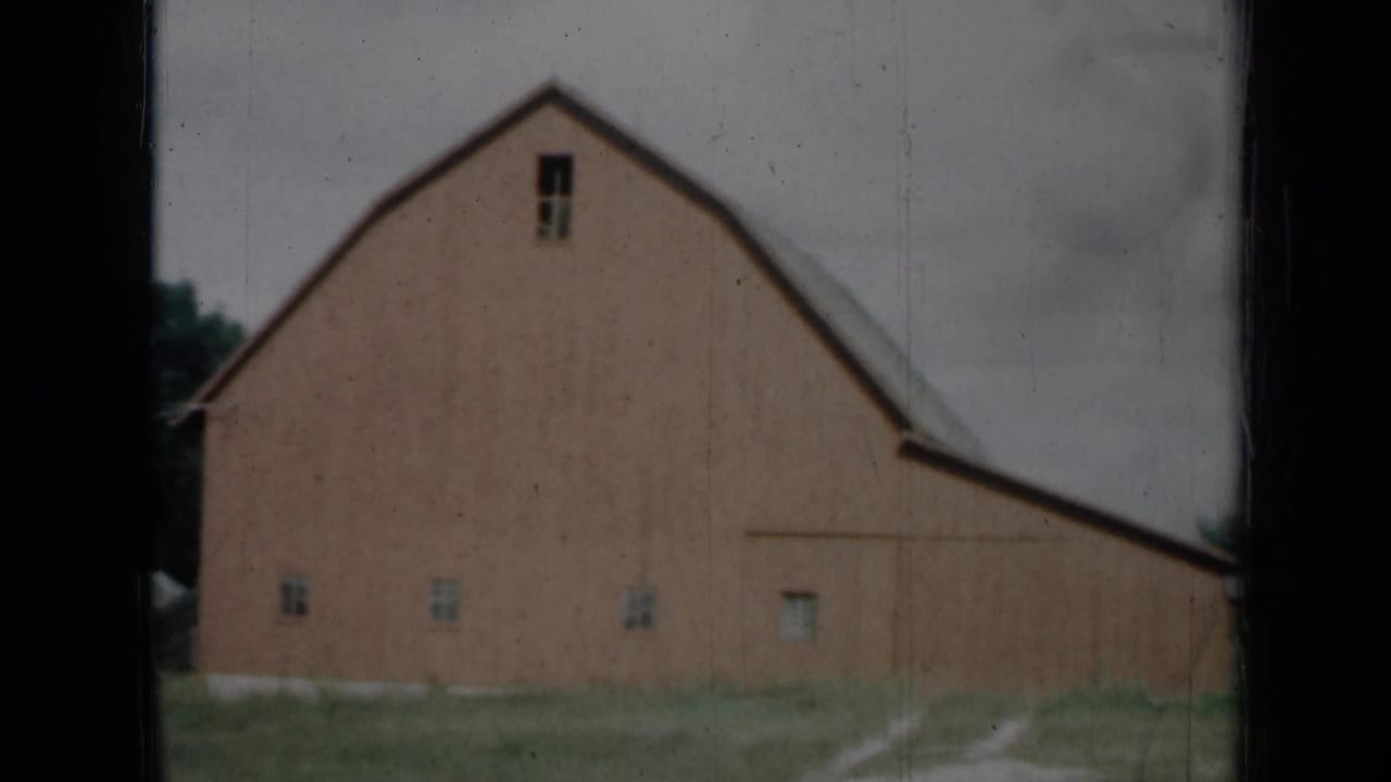 1961 Missouri rural barn exterior with weathered red siding, small windows and a pale track through grass.