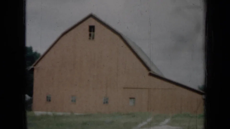 1961 Missouri rural barn exterior with weathered red siding, small windows and a pale track through grass.