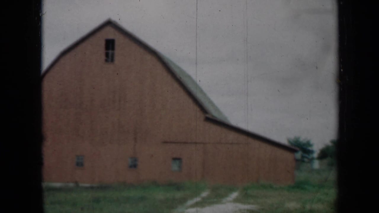 1961 Missouri 8mm frame showing the barn side, gambrel roofline, small windows and rough grass.