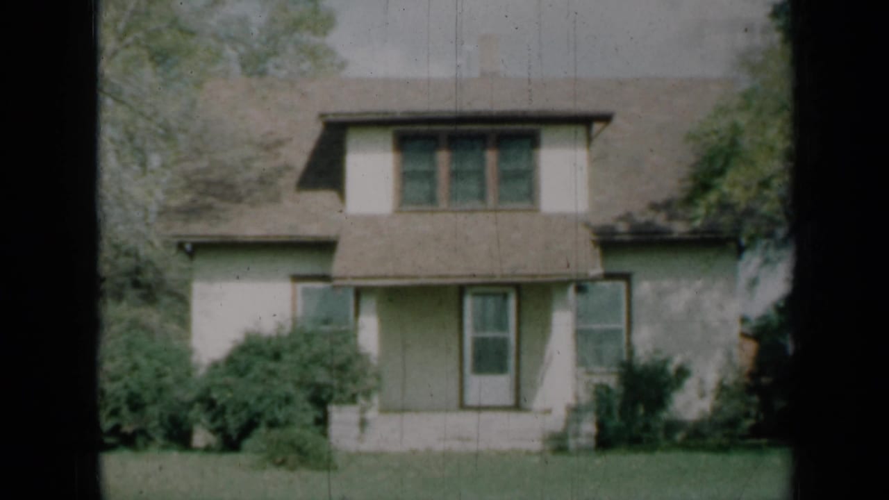 1961 Missouri home-movie view of a modest white house with brown trim, covered porch, shrubs and lawn.