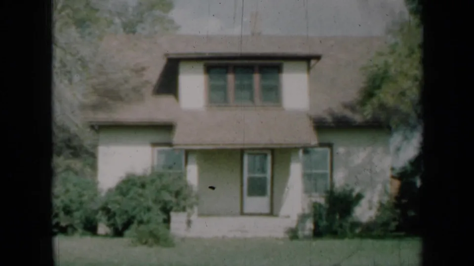 1961 Missouri 8mm frame showing the same two-story residential facade with shaded porch, windows, shrubs, and lawn.