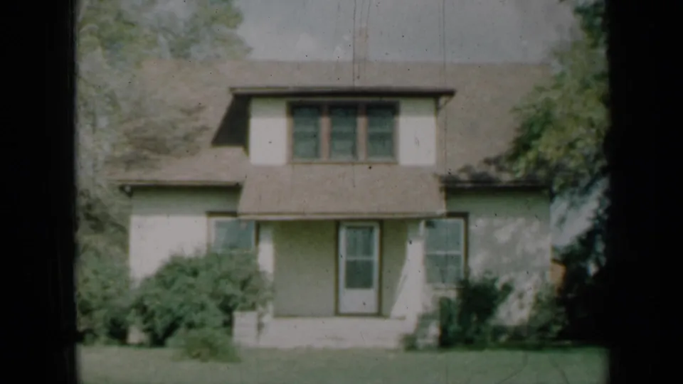 1961 Missouri frame of a two-story suburban house framed by trees, showing a porch, front door, windows, shrubs, and lawn.