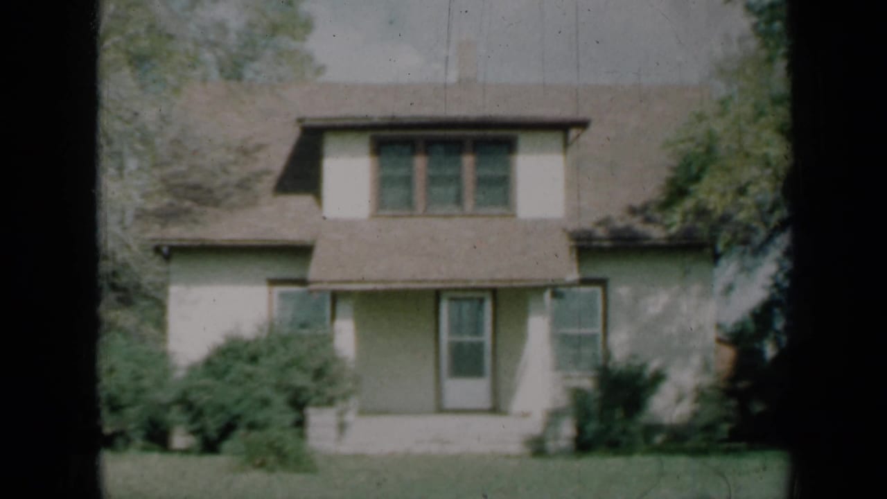 Two-story house facade with three upper windows, central door, shrubs, and lawn.