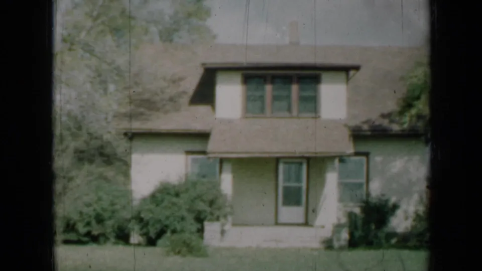 1961 Missouri 8mm frame of a two-story suburban house with a dormer, central entry, front windows, shrubs, and a grassy lawn.
