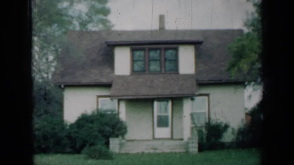 1961 Missouri 8mm frame showing the same two-story house, central dormer, front steps, low shrubs, open lawn and trees.