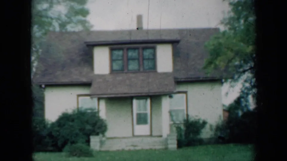 1961 Missouri 8mm frame showing a light two-story house with a dormer, front entry, porch steps, shrubs, and lawn.