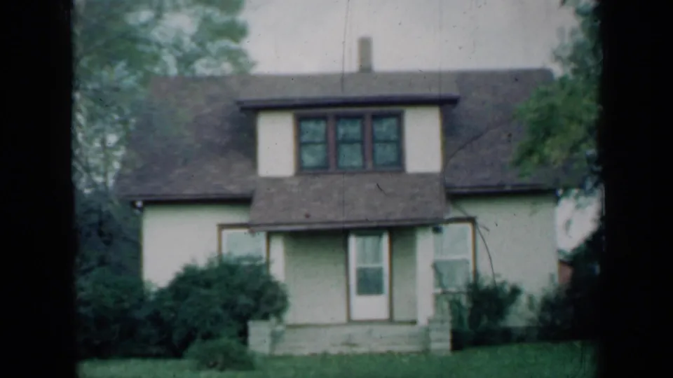 1961 Missouri 8mm still of a residential front facade with dormer windows, porch steps, bushes, lawn, and visible film gate edges.