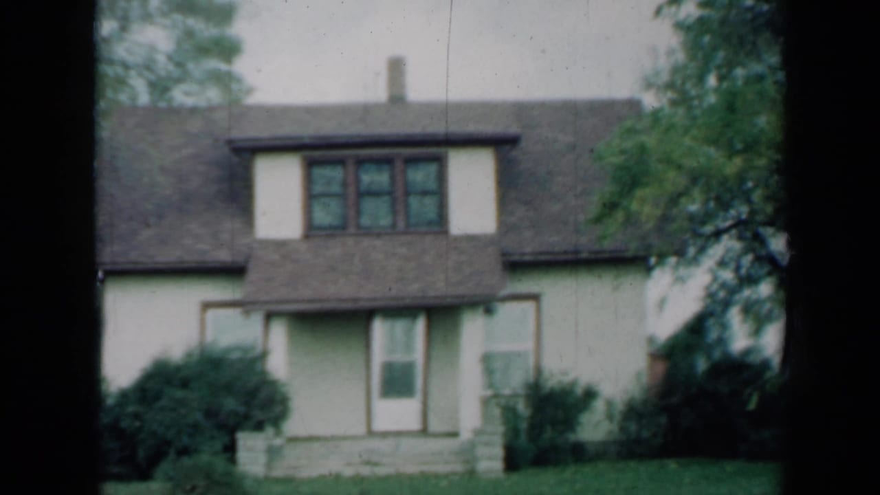Two-story house with white siding, dark roof, lawn, shrubs, and trees.