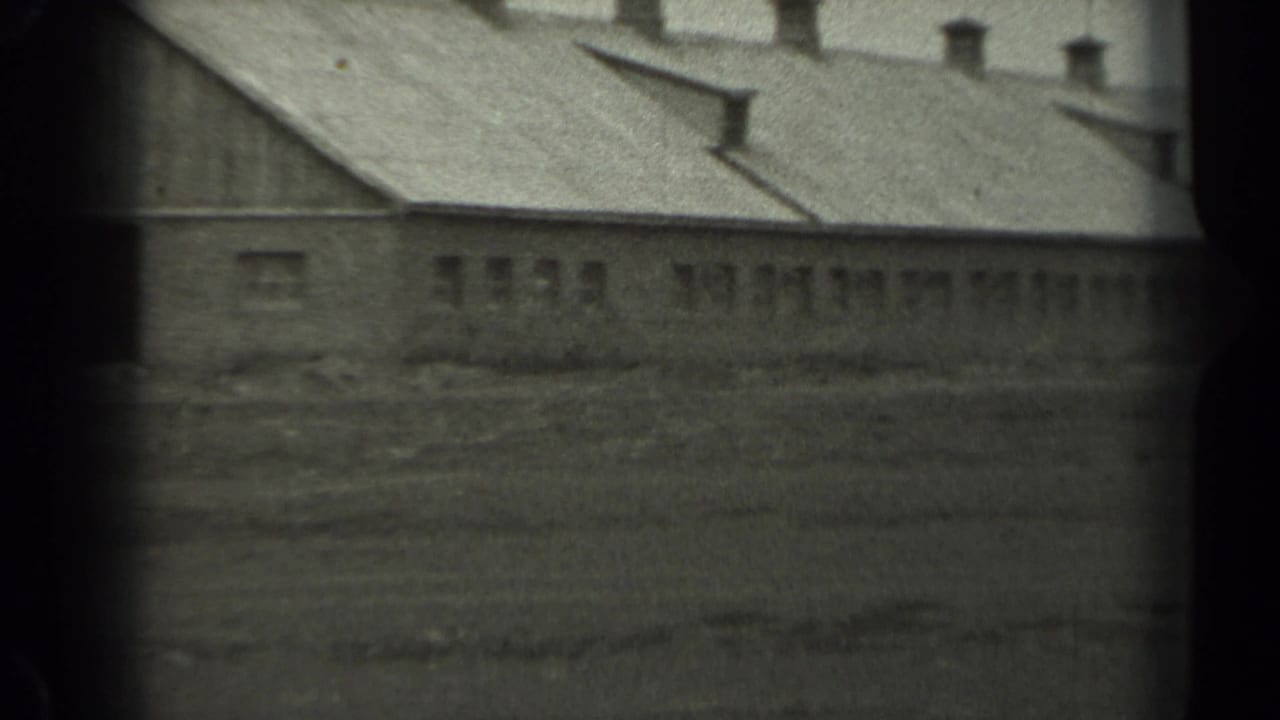 Black-and-white 8mm frame of a long rural building in Missouri, with roof vents, small windows, and empty open ground.