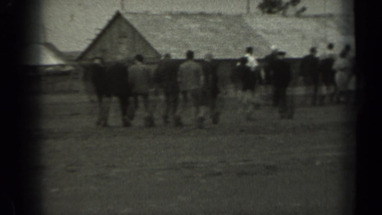 In rural Missouri home-movie footage from 1961, adults walk across open ground toward low wooden structures.