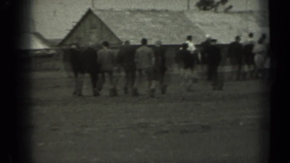 In rural Missouri home-movie footage from 1961, adults walk across open ground toward low wooden structures.